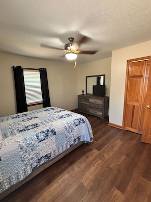 A bedroom with a bed, a dresser, a mirror, a ceiling fan, and a door.