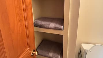 A bathroom with a toilet, a wooden door, and a shelf unit with folded towels.