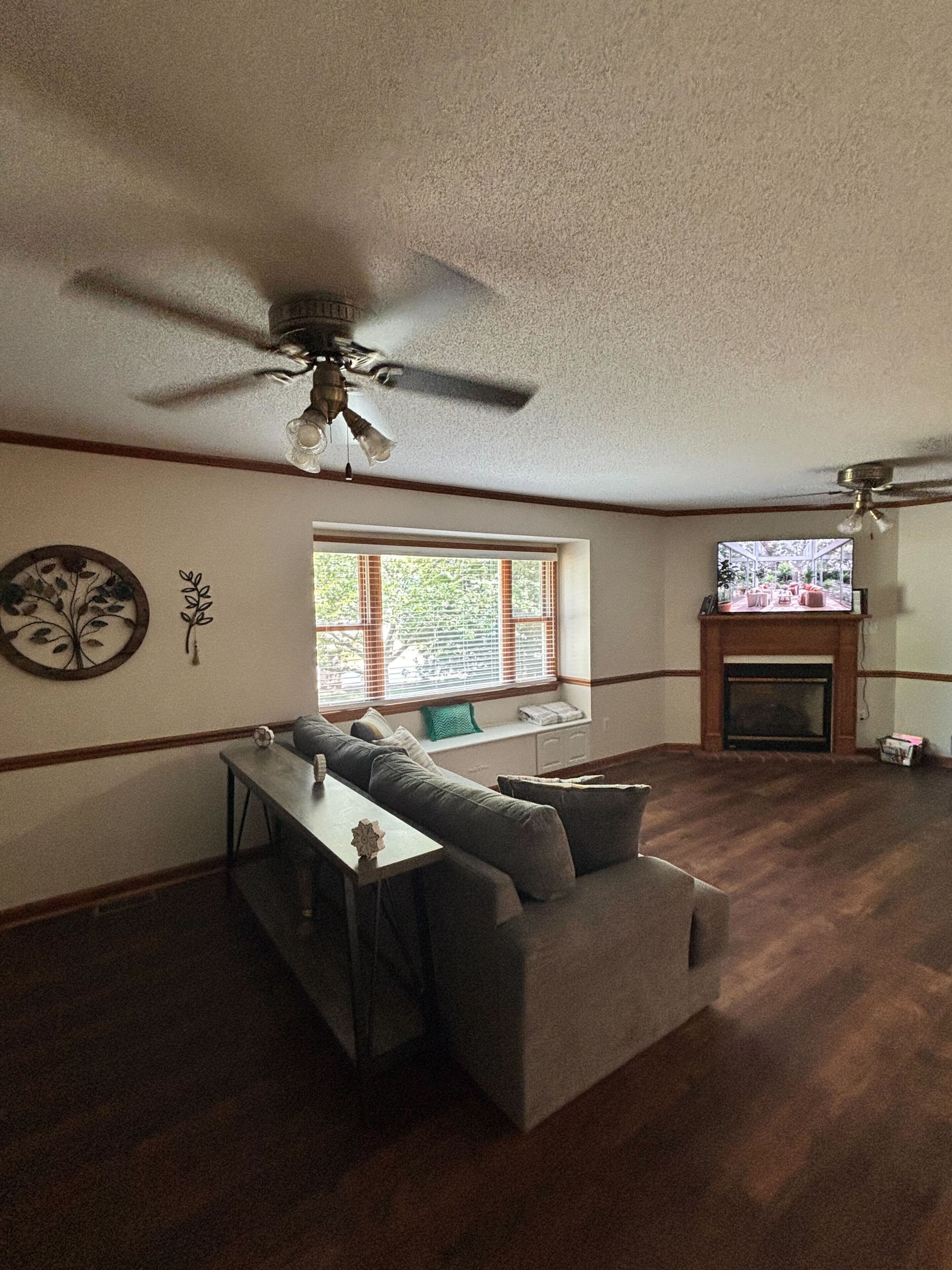 Un salon avec un ventilateur de plafond, un canapé, une table et une cheminée.