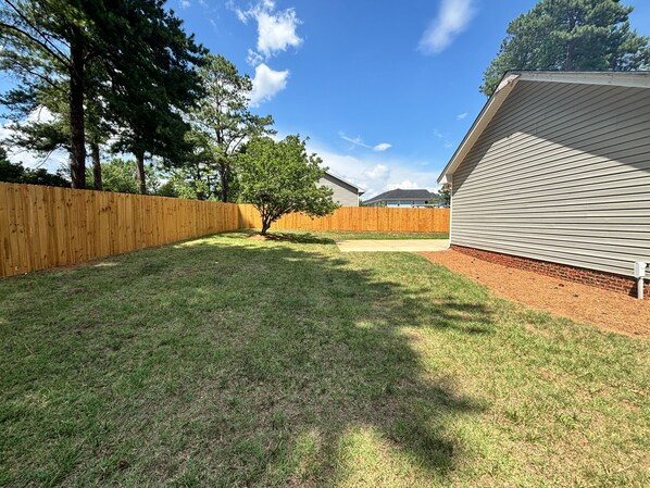 A backyard with a wooden fence, a tree, and a house with a sloped roof.