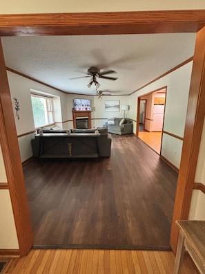 A spacious living room with a fireplace, a ceiling fan, and a view into the kitchen.