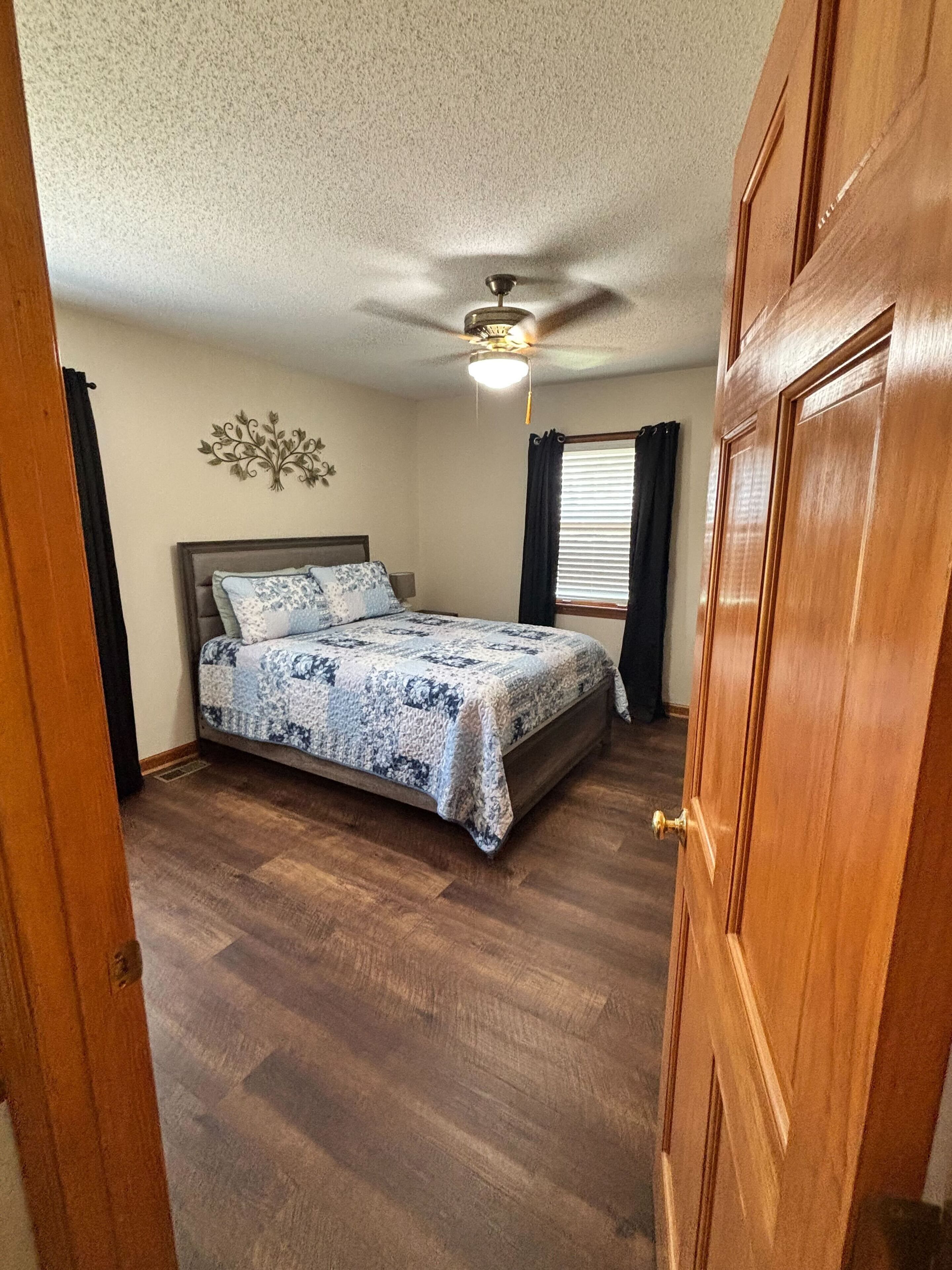 Un dormitorio con cama, ventilador de techo y puerta de madera.