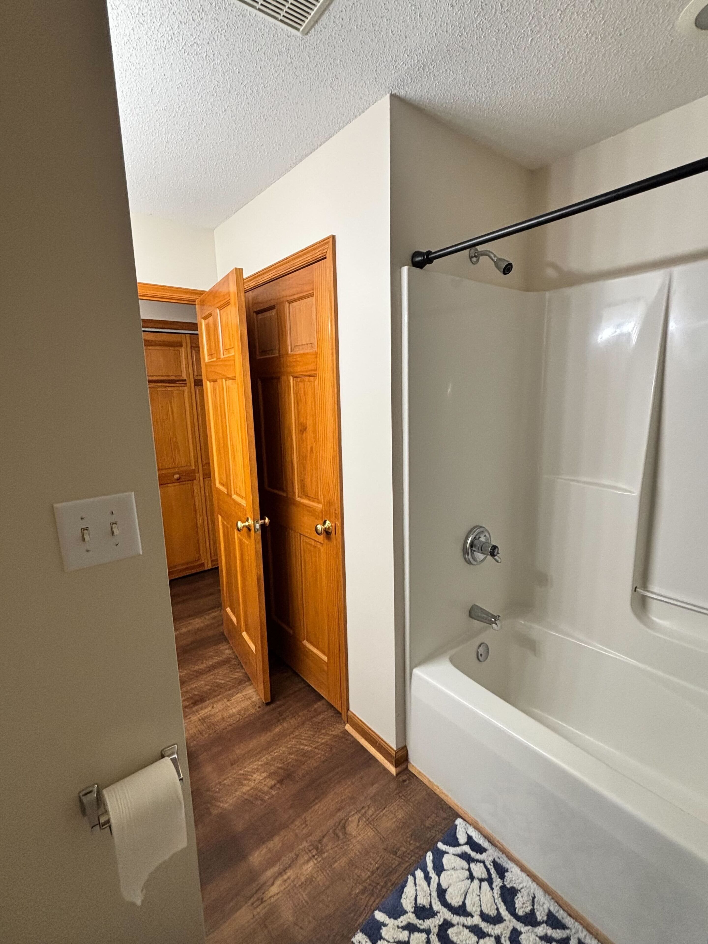 A bathroom with a bathtub, a shower, and a wooden door leading to a hallway.