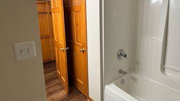 A bathroom with a bathtub, a shower, and a wooden door leading to a hallway.