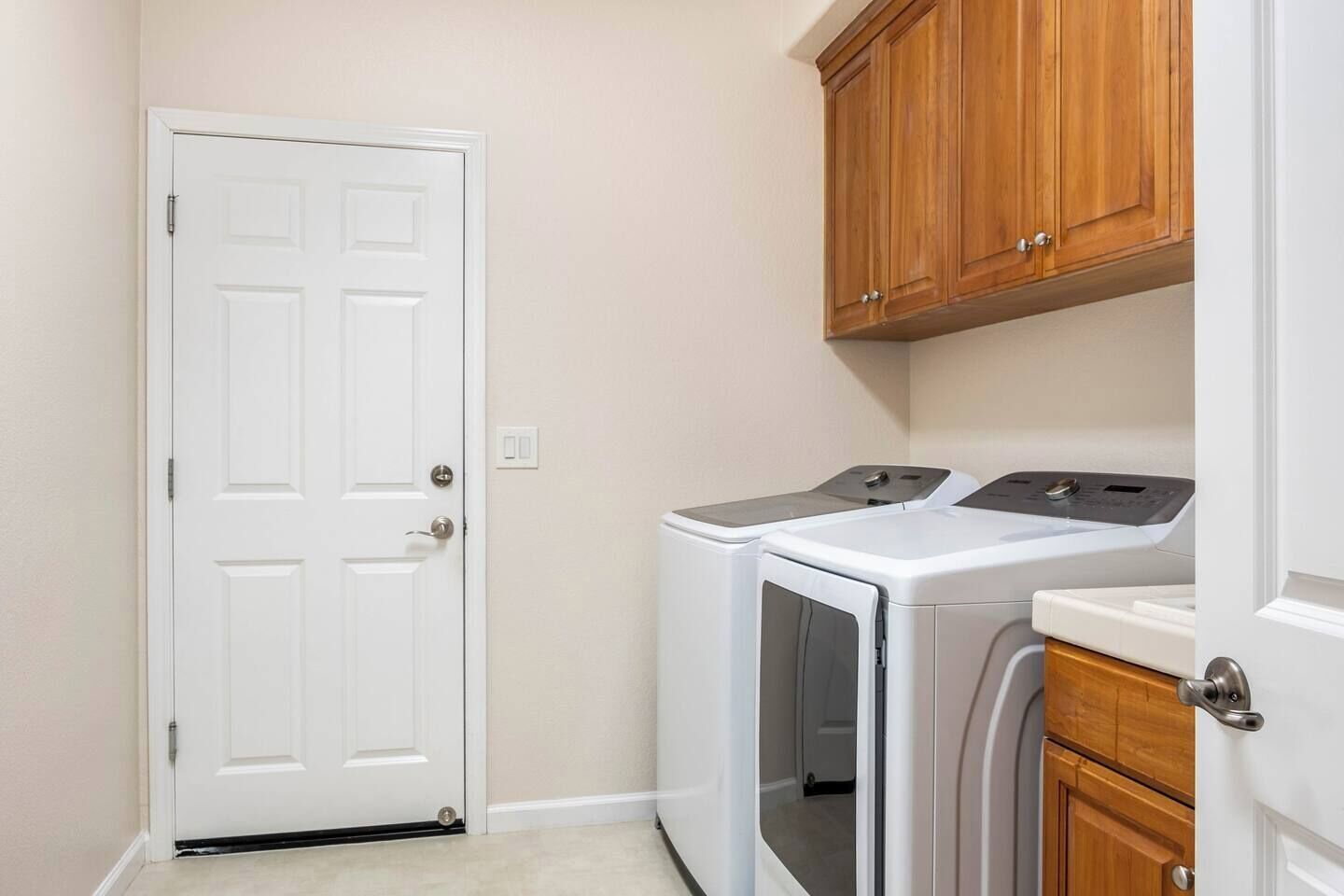 Une buanderie avec une porte blanche, un lave-linge, un sèche-linge, des armoires en bois et un plan de travail.