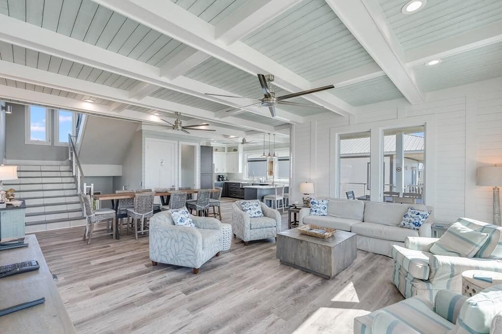 A spacious living area with a high ceiling, multiple seating arrangements, and a kitchen in the background.