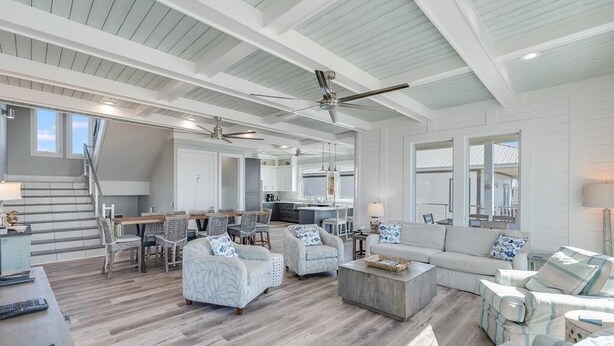 A spacious living area with a high ceiling, multiple seating arrangements, and a kitchen in the background. - Singing Waves (Port St. Joe)