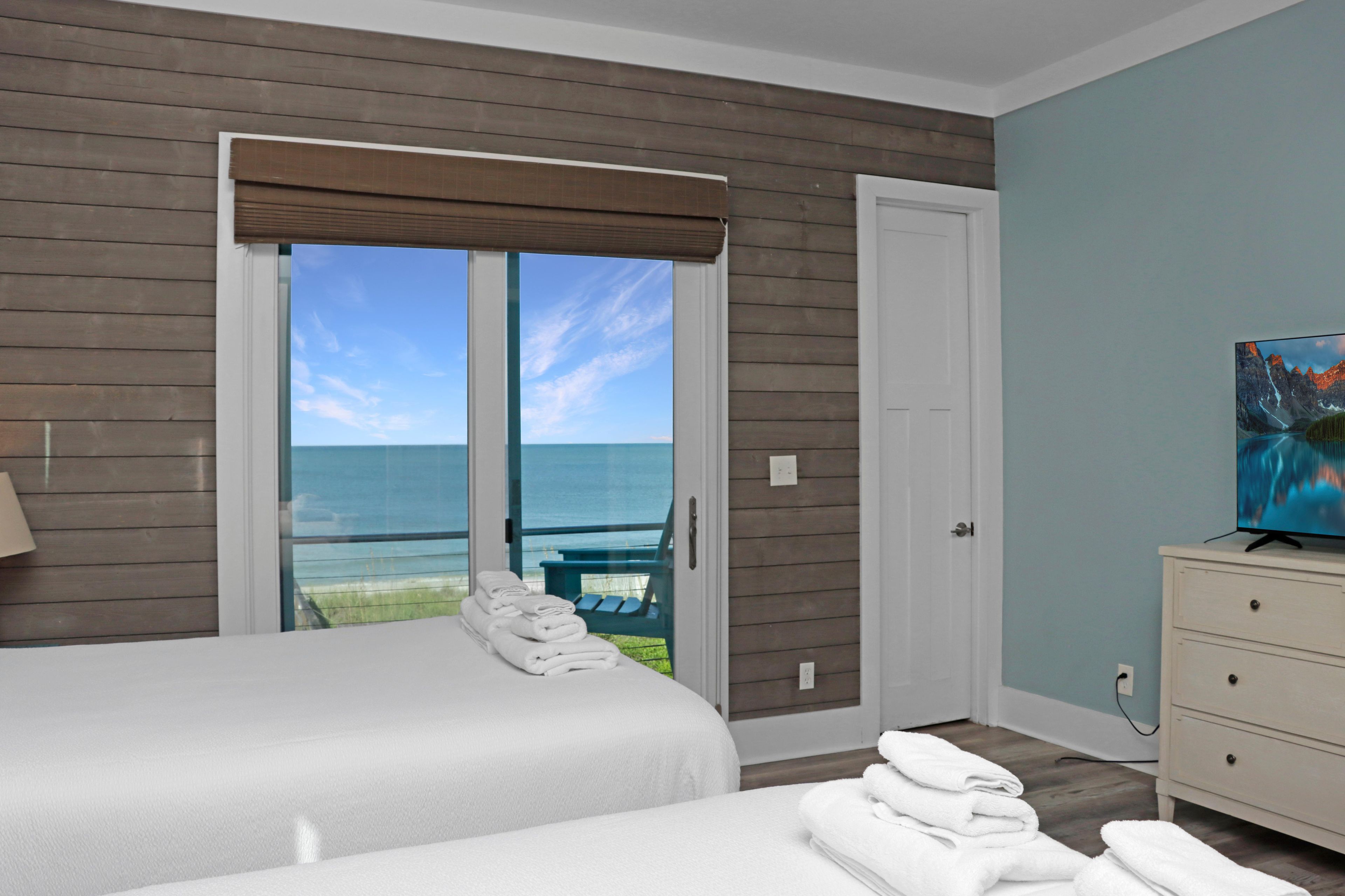 A hotel room with a bed, a chair, a painting, and a view of the ocean.