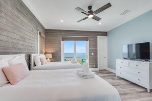 A bedroom with two beds, a ceiling fan, a TV, and a view of the ocean. - Singing Waves (Port St. Joe)