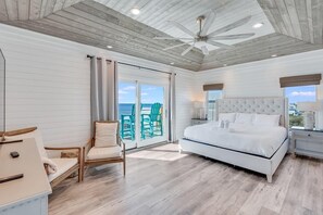 Ein Schlafzimmer mit einem großen Bett, einem Sessel, einem Schreibtisch und Meerblick durch eine Schiebetür.