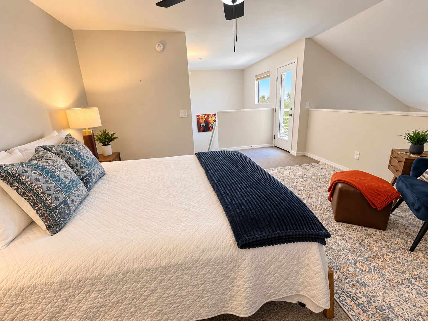 A bedroom with a bed, a nightstand, a lamp, a window, and a door.
