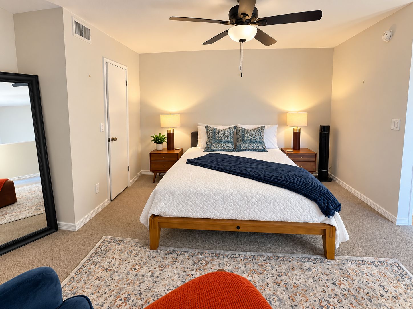 A bedroom with a bed, bedside lamps, a ceiling fan, and a large mirror.