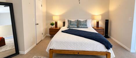 A bedroom with a bed, bedside lamps, a ceiling fan, and a large mirror.