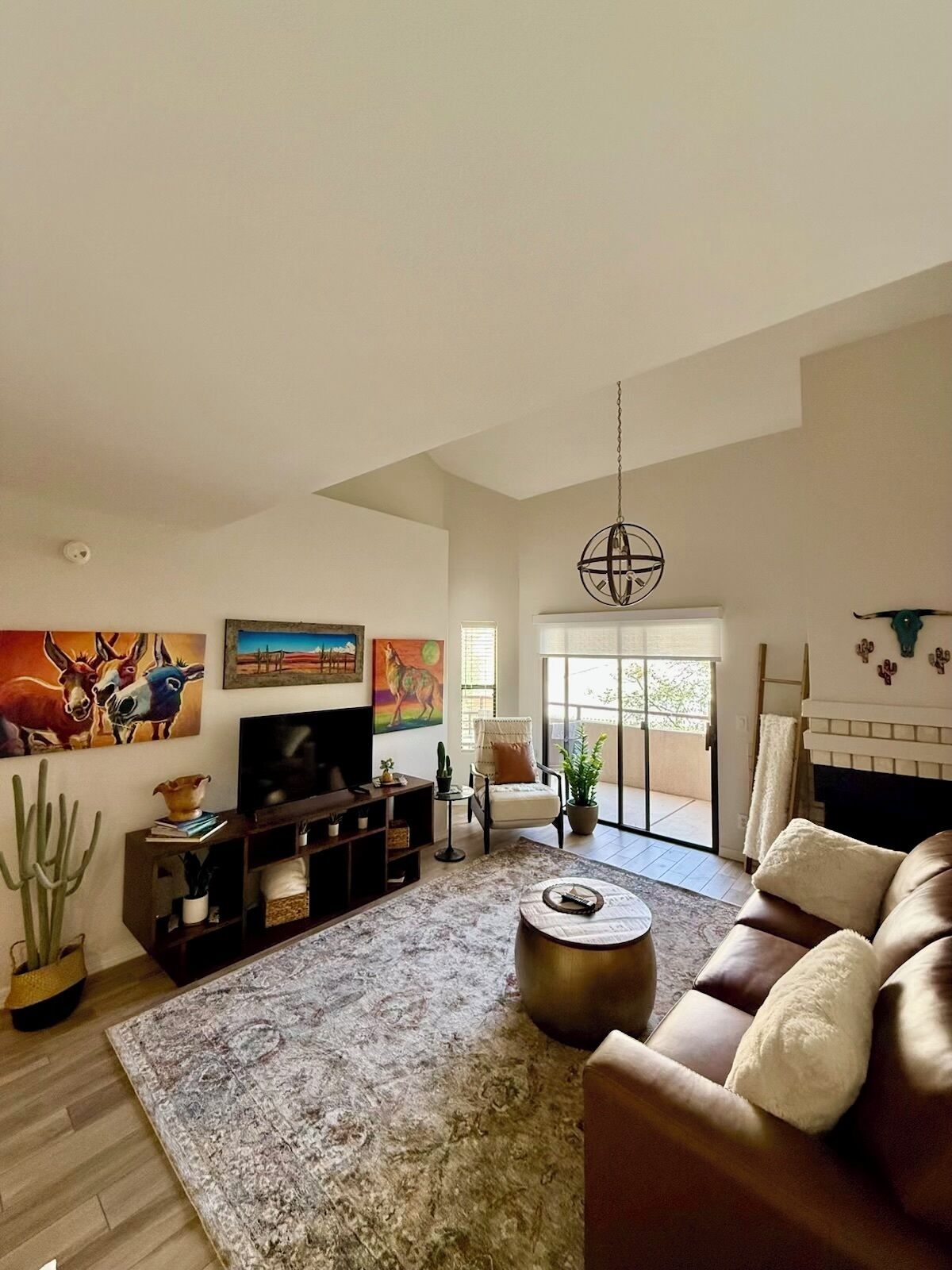 A spacious living room with a brown leather sofa, a coffee table, a television, and artwork on the walls.