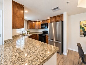 A kitchen with granite countertops, stainless steel appliances, wooden cabinets, and a black chair. - Modern Villa+ Scottsdale Resort + Pool + Golf Course+ Walking paths +Gym +Dining (Scottsdale)