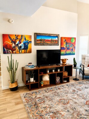 A living room with a flat-screen TV, a wooden entertainment unit, a patterned rug, and three paintings on the wall. - Modern Villa+ Scottsdale Resort + Pool + Golf Course+ Walking paths +Gym +Dining (Scottsdale)