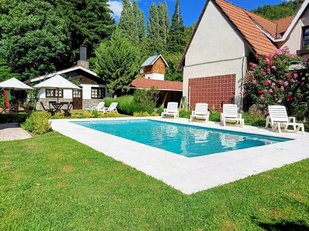 Una piscina con sillas de descanso, rodeada de un césped cuidado y una casa con techo de tejas.