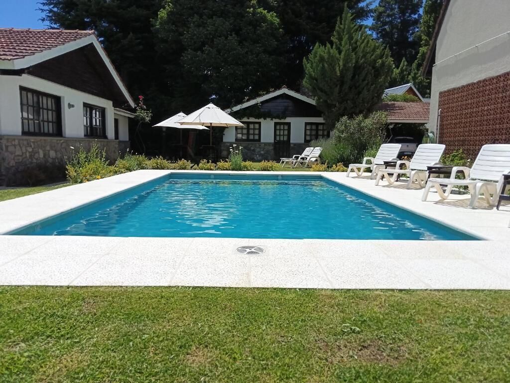 Una piscina rectangular con borde blanco, rodeada de césped y una fila de sillones blancos.