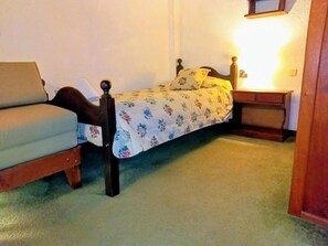 Una cama individual con una colcha estampada, una mesita de noche con lámpara y una silla.