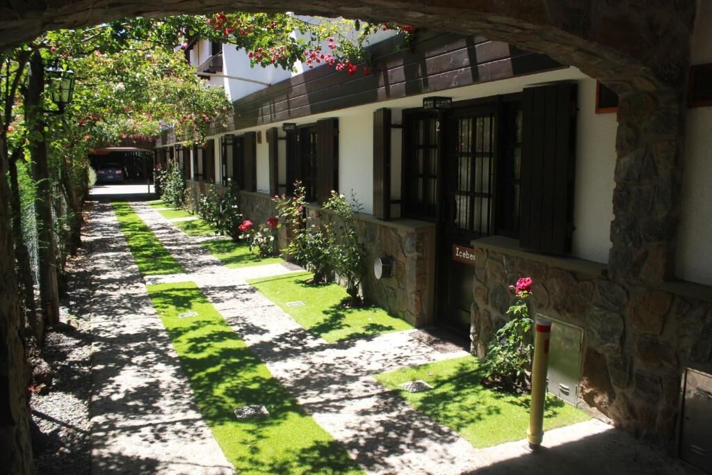 Un pasillo con piso a cuadros, paredes de piedra y una hilera de ventanas con contraventanas.