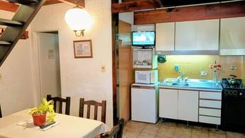 Une cuisine compacte équipée d’un four à micro-ondes, d’un évier et d’une cuisinière. On y trouve une table à manger avec des chaises et une plante en pot. Un téléviseur est fixé au mur.
