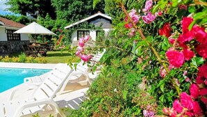 A pool area with white lounge chairs and a house in the background.