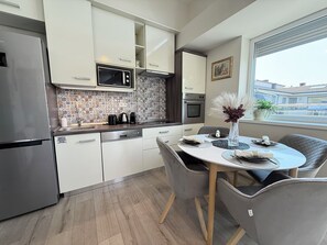 Een moderne keuken met witte kastjes, een roestvrijstalen koelkast, een magnetron en een oven. Er staat een eettafel met stoelen en een vaas met bloemen.