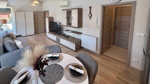 A modern living room with a sofa, dining table, and a TV. There are pendant lights, a clock, and a door. - Penthouse with a Panorama balcony, and free Parking! (Kecskemét)
