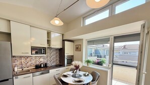 A modern kitchen with a dining area, featuring a large window with a view of buildings and a balcony. - Penthouse with a Panorama balcony, and free Parking! (Kecskemét)