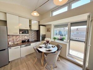 A modern kitchen with a dining area, featuring a large window with a view of buildings and a balcony. - Penthouse with a Panorama balcony, and free Parking! (Kecskemét)