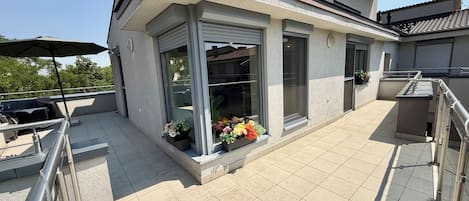 A modern building with a balcony, outdoor seating, and potted plants.