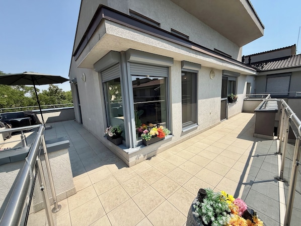 A modern building with a balcony, outdoor seating, and potted plants.