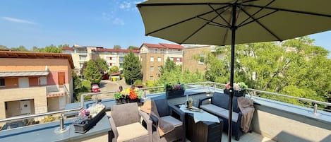 Una terraza en la azotea con mobiliario exterior, una sombrilla grande y plantas en macetas.