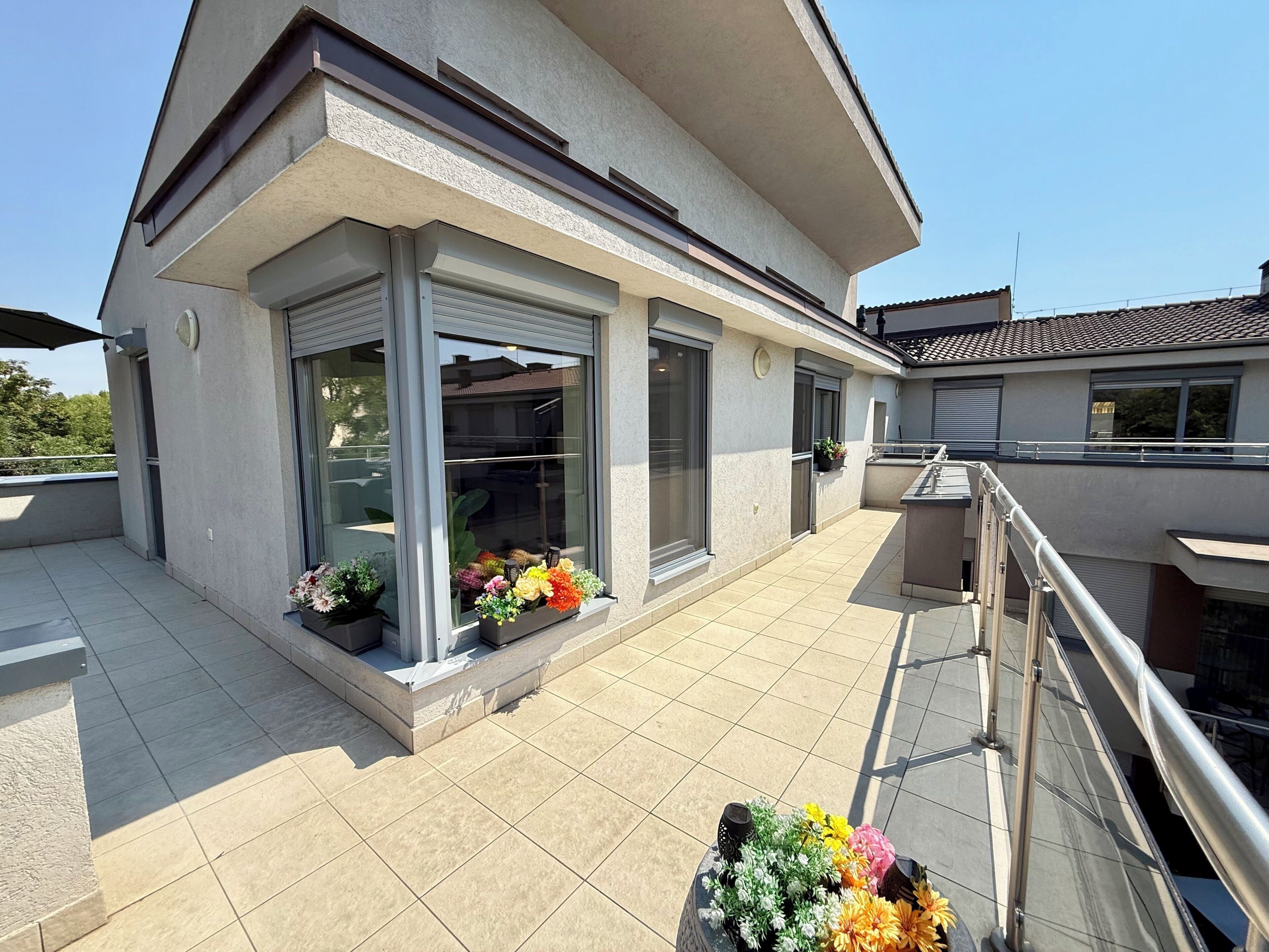 Ein modernes Gebäude mit Balkon, großen Fenstern und Blumentöpfen.