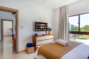 Ein Hotelzimmer mit Bett, Wandfernseher, Vorhängen am Fenster und Blick ins Freie.