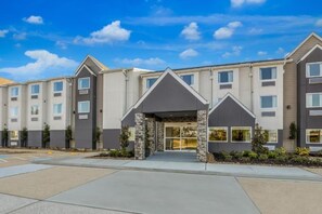 A multi-story hotel with a central entrance, a parking lot, and a clear sky.