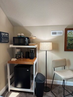 A compact kitchenette with a microwave, coffee maker, and storage containers. A trash bin and a chair are also visible. - A Room in a Lake and Mountain Town (Coeur d'Alene)