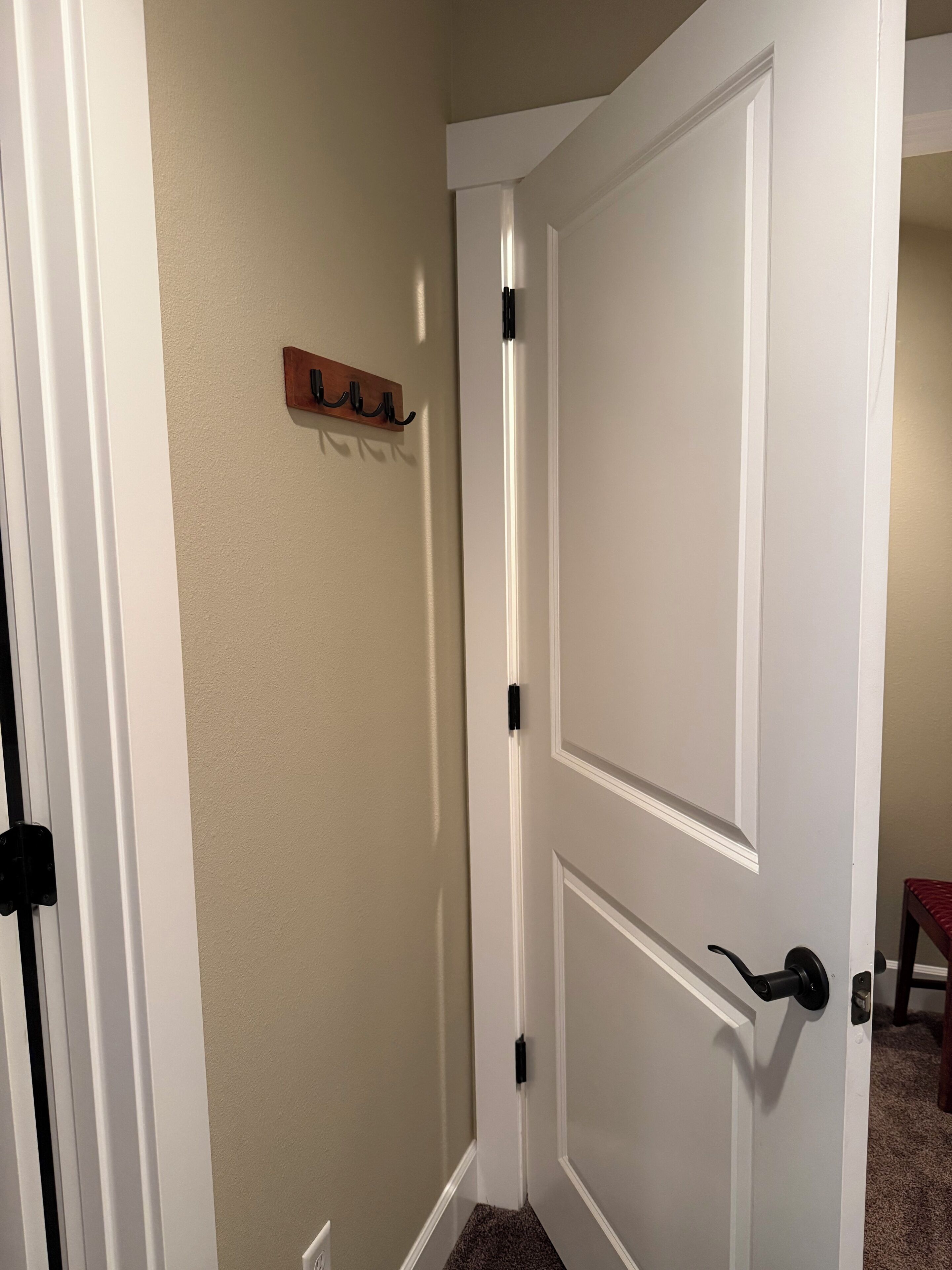 Una puerta blanca cerrada con un picaporte negro y un perchero de madera con ganchos en la pared.