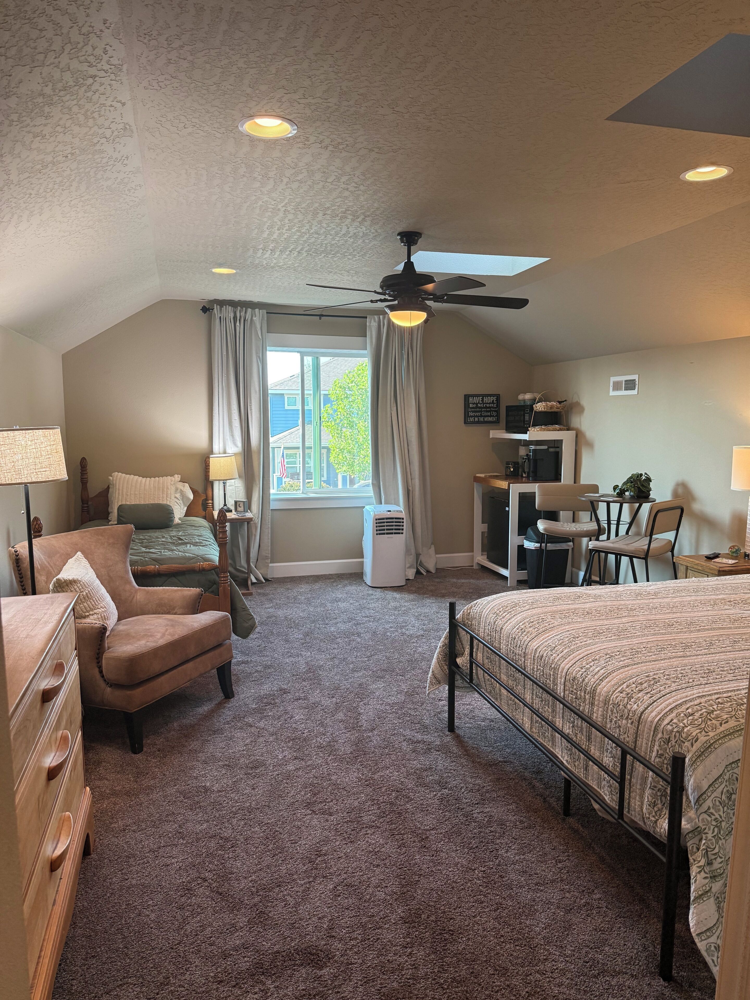A bedroom with a bed, a chair, a desk, a ceiling fan, and a window with curtains.