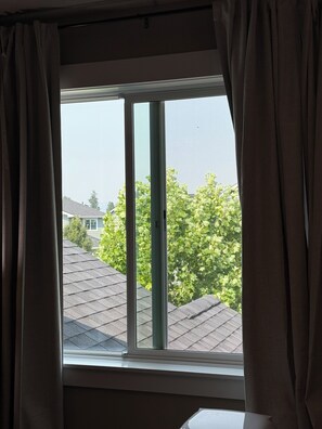 Een raam met gordijnen, uitzicht op een woonwijk met bomen en een huis.