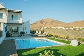 Ein modernes, zweistöckiges Haus mit Swimmingpool, Gartenmöbeln und Blick auf einen Berg.