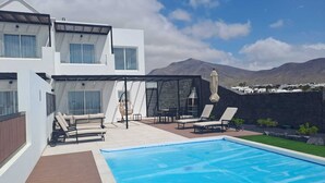 Et moderne hus med to etager, en swimmingpool, udendørs siddepladser og udsigt til bjerge.