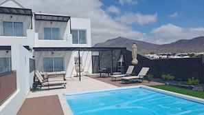 Ein modernes, zweistöckiges Haus mit Swimmingpool, Sitzgelegenheit im Freien und Blick auf Berge.