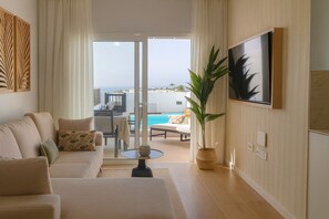 Ein Wohnzimmer mit Sofa, Couchtisch und Topfpflanze. Es gibt einen Essbereich mit Tisch und Stühlen sowie Blick auf Pool und Landschaft.