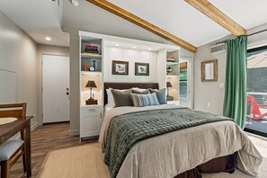 A bedroom with a bed, built-in shelving, a desk, and a window with curtains. - Timber & Tide: Two-Space Woodland Retreat (Saugatuck)