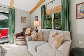 A living room with a sofa, two chairs, a lamp, and a window with curtains. - Timber & Tide: Two-Space Woodland Retreat (Saugatuck)