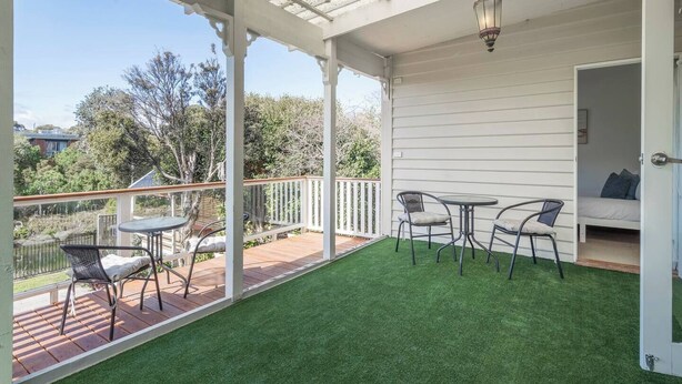 Overdekt terras met tafel en stoelen, een deur naar een slaapkamer, en uitzicht op de omgeving.