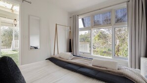 Een slaapkamer met een bed, een hangstoel, een groot raam en uitzicht op de natuur.