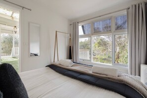 A bedroom with a bed, a hanging chair, a large window, and a view of the outdoors. - Willow Landing Beach House with Private Jetty (Frankston)