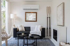 A modern living room with a black sofa, a round coffee table, a floor lamp, and a fireplace. - Willow Landing Beach House with Private Jetty (Frankston)